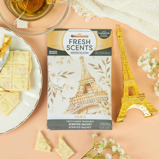 The Fresh Scents Paris - Sachet 3pk features an Eiffel Tower design, displayed on a peach surface with white chocolate, a gold Eiffel Tower figurine, and a teacup—ideal flameless air fresheners for long-lasting fragrance.