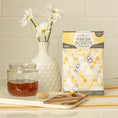 Load image into Gallery viewer, A honey jar with dipper, bee figurine, white vase with daisies, and Fresh Scents Bee Happy - Sachet 3pk featuring bee and honeycomb designs create a charming kitchen display with lasting fragrance.
