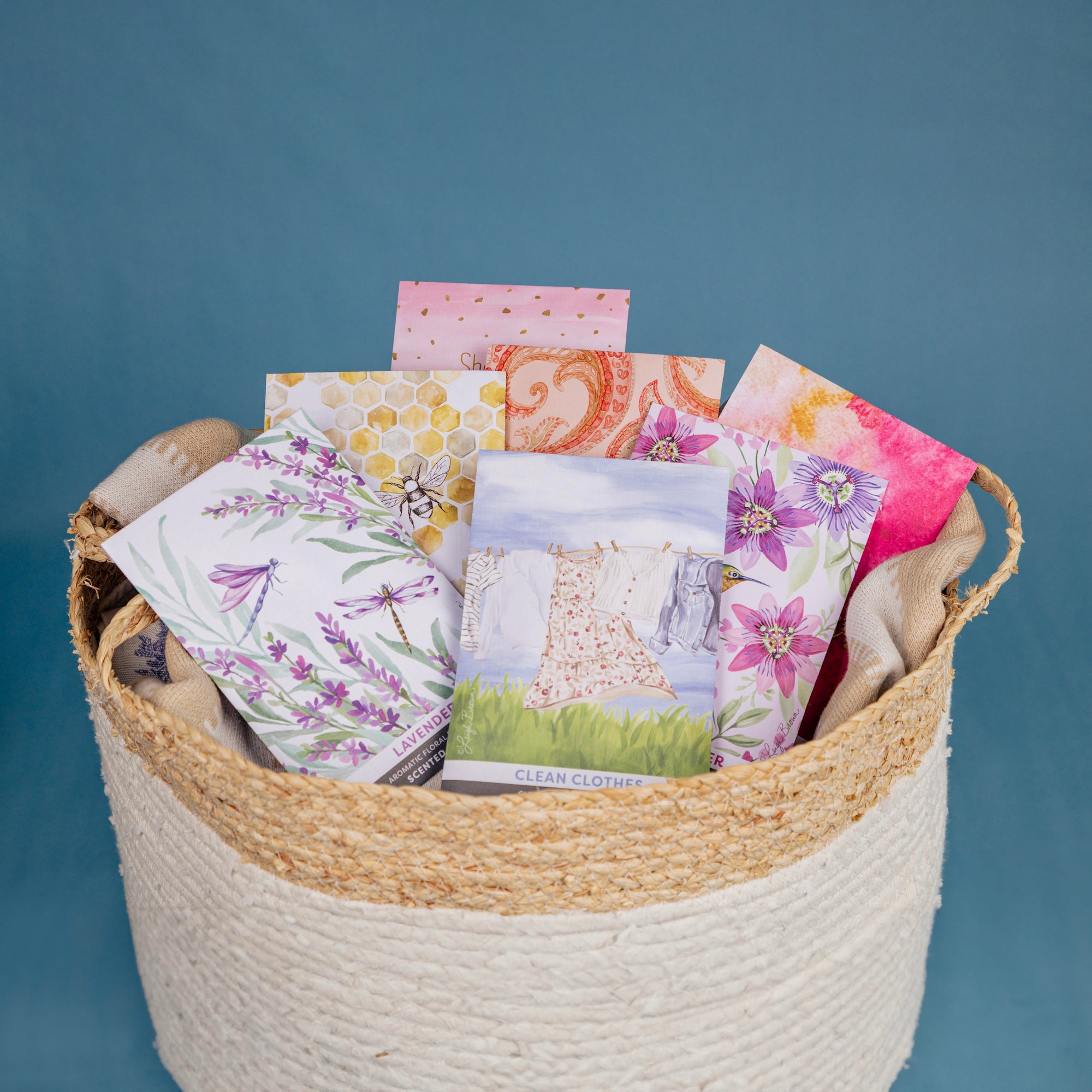 A woven basket containing several colorful, illustrated seed packets with floral and nature designs, set against a plain blue background.