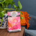 Load image into Gallery viewer, A Fresh Scents Hello Gorgeous - Sachet 3pk sits on a wooden table by a potted plant, offering long-lasting fragrance as a flameless air freshener. A blue sofa and orange pillow are visible in the background.

