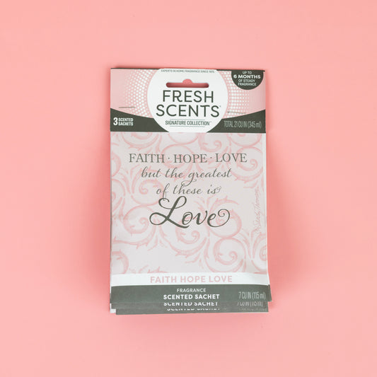 The Fresh Scents Faith Hope Love Sachet 3pk features pink air freshener sachets with floral designs and the phrase "Faith · Hope · Love but the greatest of these is Love." Enjoy long-lasting fragrance in any space.