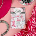 Load image into Gallery viewer, Fresh Scents Disco Cowgirl - Sachet 2pk sits on a pink background, surrounded by a red cowboy hat, silver horseshoe, disco ball, and red bandana—the perfect flameless air freshener for any small space!.