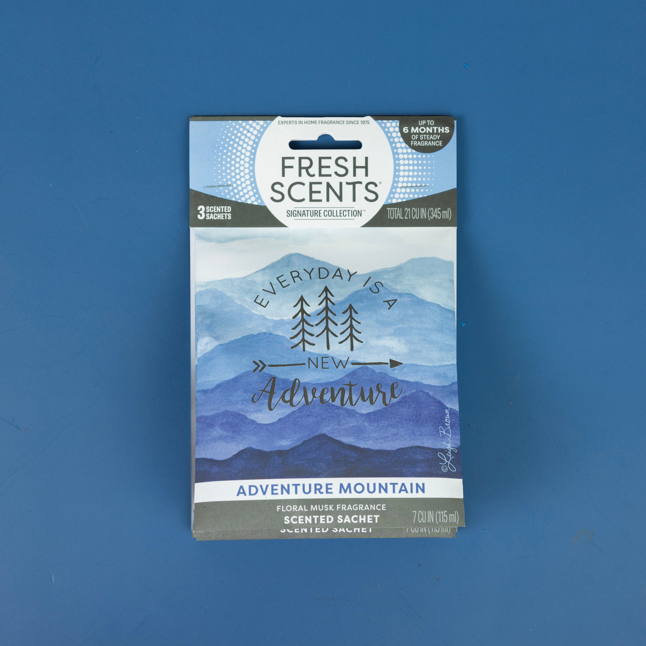A Fresh Scents Adventure Mountain - Sachet 3pk, featuring blue mountain artwork and the phrase "Everyday is a new adventure," rests on a blue surface, emphasizing long-lasting freshness.