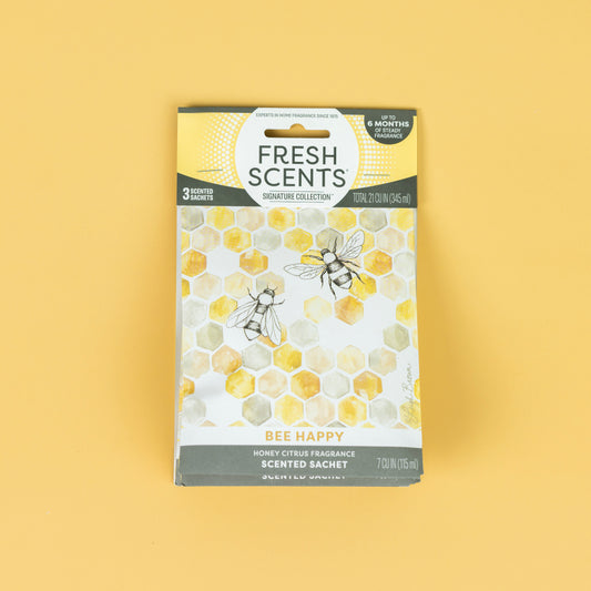 The Fresh Scents Bee Happy - Sachet 3pk features a honeycomb and bee design on yellow, with a honey citrus flameless fragrance. Each pack contains three long-lasting air freshener sachets that last up to six months.