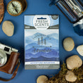 Load image into Gallery viewer, A Fresh Scents Adventure Mountain - Sachet 3pk, promising lasting freshness, is displayed with travel items such as a camera, compass, and flashlight on a blue background. The package features the phrase "Everyday is a new adventure.