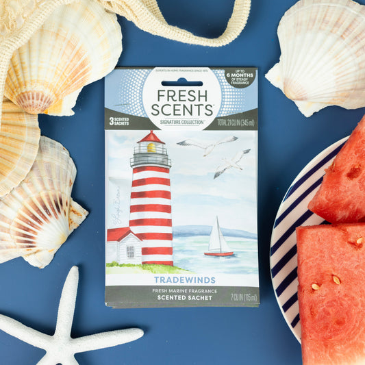 The Tradewinds - Sachet 3pk by Fresh Scents features a charming lighthouse, seagulls, and sailboat design with seashells and watermelon slices—a flameless air freshener for long-lasting fragrance on a blue background.
