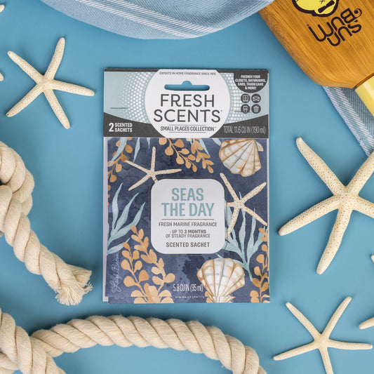 The Fresh Scents Seas the Day - Sachet 2pk is shown on a blue background with starfish, a rope, and a wooden brush. Each sachet displays sea-themed designs—perfect for adding fragrance to small spaces.