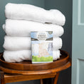 Load image into Gallery viewer, A stack of towels on a stool is complemented by Fresh Scents’ Clean Clothes Sachet 3pk, adding a gentle, flameless fragrance to your space.