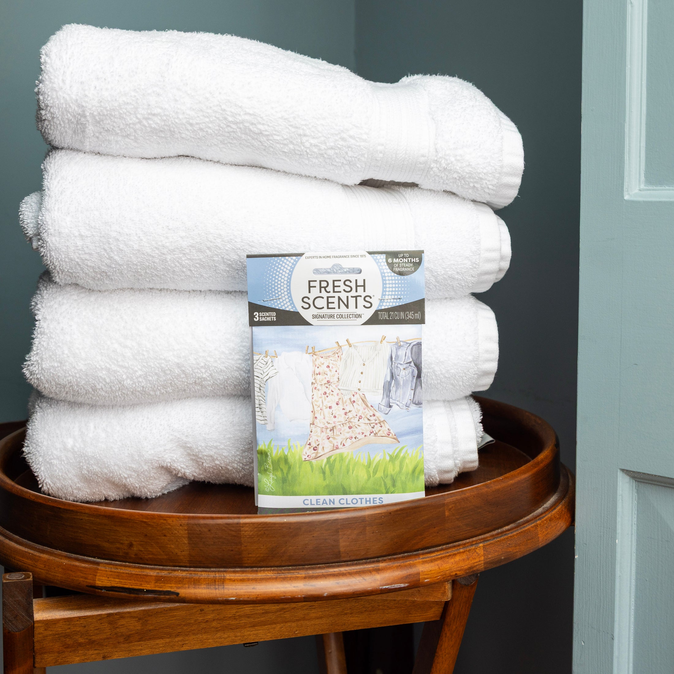 A stack of towels on a stool is complemented by Fresh Scents’ Clean Clothes Sachet 3pk, adding a gentle, flameless fragrance to your space.